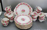 Full display of the pink roses English china tea set including stacked plates, cups, saucers, and larger cake plate.