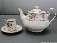 Full view of Royal Albert Petite Point teapot with demitasse cup and saucer, showing floral pattern and gold trim.