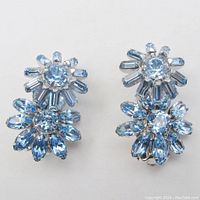 Front view of both earrings showing blue rhinestone flowers with marquise and baguette shapes mounted on silver tone metal.