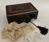 Close up of lace needlework pieces draped in front of the closed sewing box.