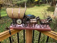 Full side view of the vintage horse buggy clock and lamp showing all four copper-colored horses, buggy with covered wagon top, clock, lamp, and copper metal base. Power cord visible with plug.