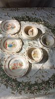 Set of 7 Bunnykins plates and bowls showing bunny illustrations and brown bunny borders on porcelain dishes.