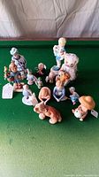 Lot displayed on green felt pool table surface showing a group of porcelain figurines and a stuffed teddy bear with violin.