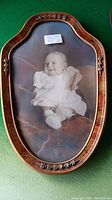 Oval wooden framed photo featuring a smiling baby in white clothing, with floral carvings on the frame.
