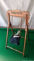 Front view of wooden swing frame with china doll seated on swing.