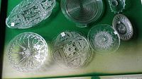 Top view of nine clear glass serving dishes with various patterns and shapes arranged on green fabric.