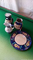 Photo showing Langley Ware flip lid pitcher, two decorative pitchers, and floral platter on green felt surface