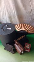 Shows black textured hard case, folding fan, black felt hat, light brown woven purse, small brown leather coin purse, and small framed photo