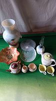 Overview of lot items including tea set, vase, glass plates, decorative dish, and oil lamp on green surface