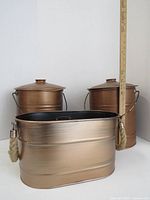 Three copper-finished metal containers with rope handles grouped together showing sizes and handles.