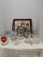 Photo showing nine collectible beer mugs with various brand logos and graphics arranged in front of the wooden serving tray.