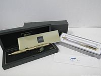 Both Cross ballpoint pens, gold-tone and silver-tone, displayed in their original boxes with packaging and documentation visible.