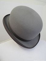 Side and top angle view of gray bowler hat without box, showing curved brim and smooth rounded crown.