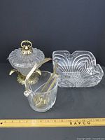 Photo showing three items: cut crystal ice bucket with metal lid and feet, metal ice bucket tongs inside the bucket, and a clear crystal bowl with swirl pattern