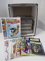 Photo showing a comic book storage box packed with approximately 70-100 bagged comics with some individual comic covers shown in front, including Dragonball #10 and Batman