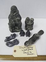 Photo showing all 8 Inuit-style soapstone or composite stone figurines together on a white surface with a ruler and handwritten tag identifying them as Wolf Original sculptures from Canada. Figurines include human figures, seals, and owl shapes.