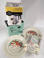 Full lot showing milk frother box, hand mixer box, two ceramic pie plates with fruit illustrations, and a pack of birthday candles.
