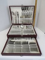 Full front view of large cutlery set open in maroon box showing all pieces organized in three levels.