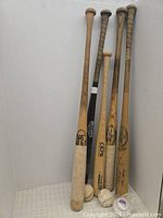 Five wooden baseball bats and four baseballs arranged upright and on the floor. Shows general wear and tape wrapped handles.