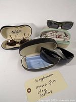 Three pairs of sunglasses displayed with their respective cases and a cleaning cloth, showing brand logos and condition.