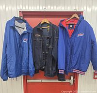 Three men's jackets hanging: blue Buffalo Bills windbreaker, dark denim Atlas For Men jacket, blue insulated Dunbrook jacket