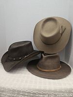 Set of three Western cowboy hats showing their overall shape and condition, one light beige, one dark brown, one brown with concho band