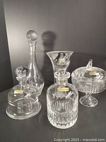 Full set of five Nachtmann crystal pieces on grey background, including three decanters, candy bowl, vase, and cheese dome, all clear crystal glass.