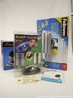 Photo showing all four items from the lot: Fellowes Laminator, Swingline Stapler, Scotch Pop-up Tape pack, and Tile Tracker, arranged together on white background.