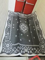 Photo showing the black side of the large woven plastic outdoor rug with white floral medallion and border pattern.