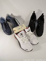 Three pairs of Puma sneakers; white with black/red, navy blue, and black pairs shown together