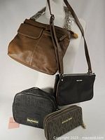 Full view of four bags showing the brown Roots leather bag, black crossbody bag, black Juicy Couture embossed bag, and Michael Kors wallet.