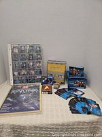 Photo showing white three-ring binder with transparent card sleeves filled with Star Trek collector cards, various Star Trek card boxes, additional loose cards, and promotional materials on table