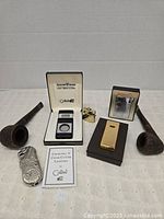 Photo of the entire collection showing two smoking pipes, four lighters including boxed Colibri Quantum SST cigar lighter & cutter, Bentley flick lighter, gold-tone lighter, and small brass lighter.
