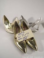 Three pairs of women's high heel shoes, showing cream/off-white, white/silver, and gold pairs