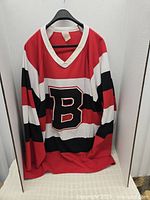 Front view of red, white, black striped hockey jersey with large letter B on front and white V-neck collar
