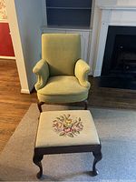 Front view of green armchair and floral upholstered ottoman on carpeted floor near fireplace and built-in bookshelf.