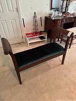 Full view of green velvet upholstered bench with wooden frame and rolled armrests in a home setting.