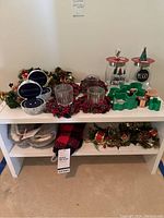 Photo showing Christmas jars, berry wreath candles, cookie cutters, and decorated votive holders on white shelf.
