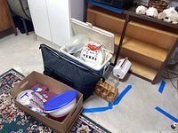 Photo shows two coolers, one black soft cooler and one white hard plastic cooler with picnic items inside and around including food storage containers and a small ice chest.