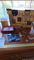 Display of costume jewelry on a table including multiple bracelets, earrings on branded cards, and pendants. Natural light from window.