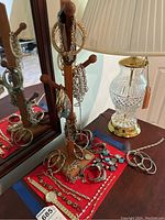 Overview of jewelry display stand with several bracelets and necklaces draped on pegs and base, alongside a glass lamp base.