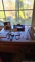 Wide view of the costume jewelry and watches displayed on a wooden surface near a window with outdoor scenery.