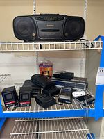 Full view of Casio stereo boombox and collection of portable electronics on shelving.