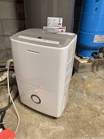 White Frigidaire humidifier placed on concrete floor near a water heater, showing front and side view.