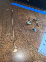 View of two gold chains with pendants and three silver pieces on wooden surface.