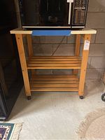 Front view of wooden kitchen cart with a smooth top surface and two slatted shelves, on casters.