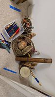 Overview of musical instruments, percussion items, baskets, and a wooden log-like instrument arranged on carpeted floor.
