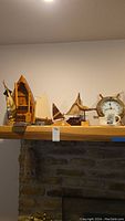 Wide view of nautical decor on wooden shelf above stone fireplace, showing various clocks, sailboat statues, and mug