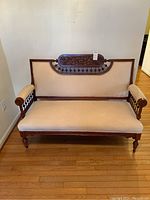 Full front view of antique wooden settee with beige upholstery and carved leaf design on backrest.