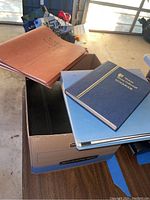 Photo of three binders/folders stacked on top of a box containing stamp collections.